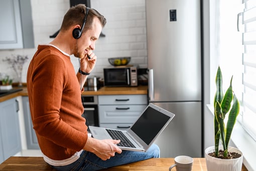 a man on his laptop taking a work phone call in his kitchen