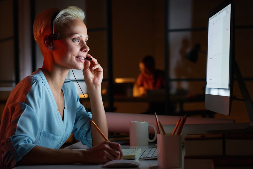 Young woman in headphones working on computer while sitting at her workplace