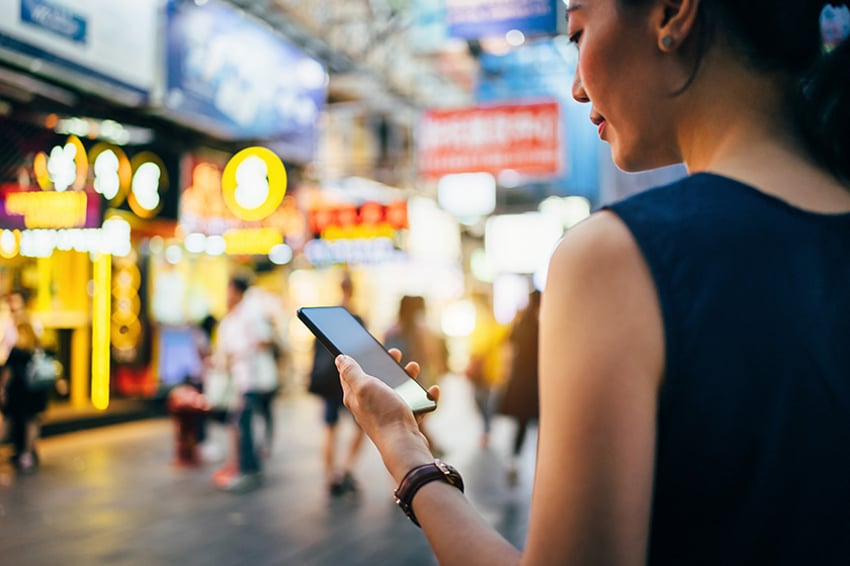 Mujer con teléfono de pie frente a unas tiendas